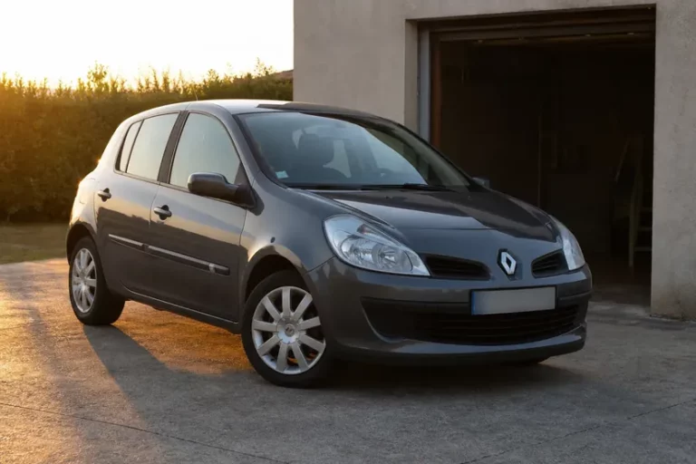 Un Ford C-Max bleu nuit garé sur l'aire bétonnée devant la porte ouverte d'un box de garage, en fin de journée.