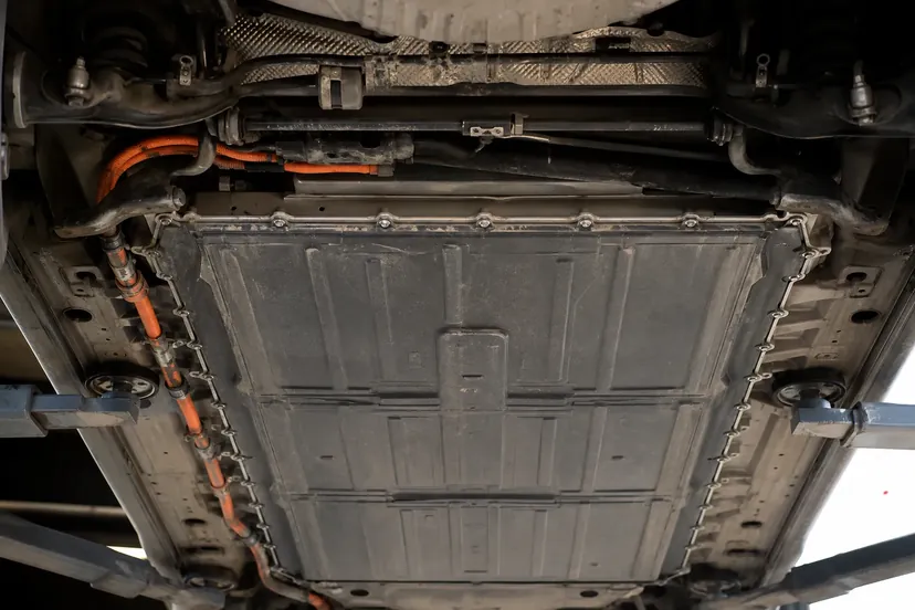 Vue en contre-plongée sur le soubassement d'une petite voiture électrique levée au pont, pack de batterie plat couvrant tout le plancher entre les essieux