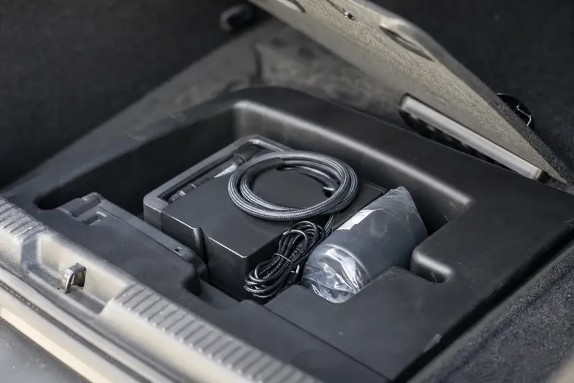 Un kit de réparation anti-crevaison, petit compresseur et cartouche de produit, logé dans la niche du plancher de coffre d'une citadine