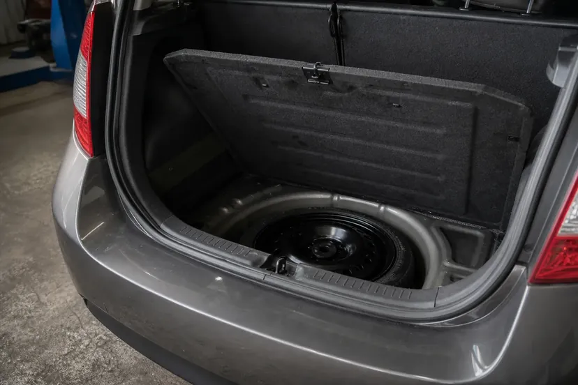 Coffre ouvert d'une petite voiture, plancher relevé, roue de secours de dépannage temporaire à pneu étroit logée dans sa cuve