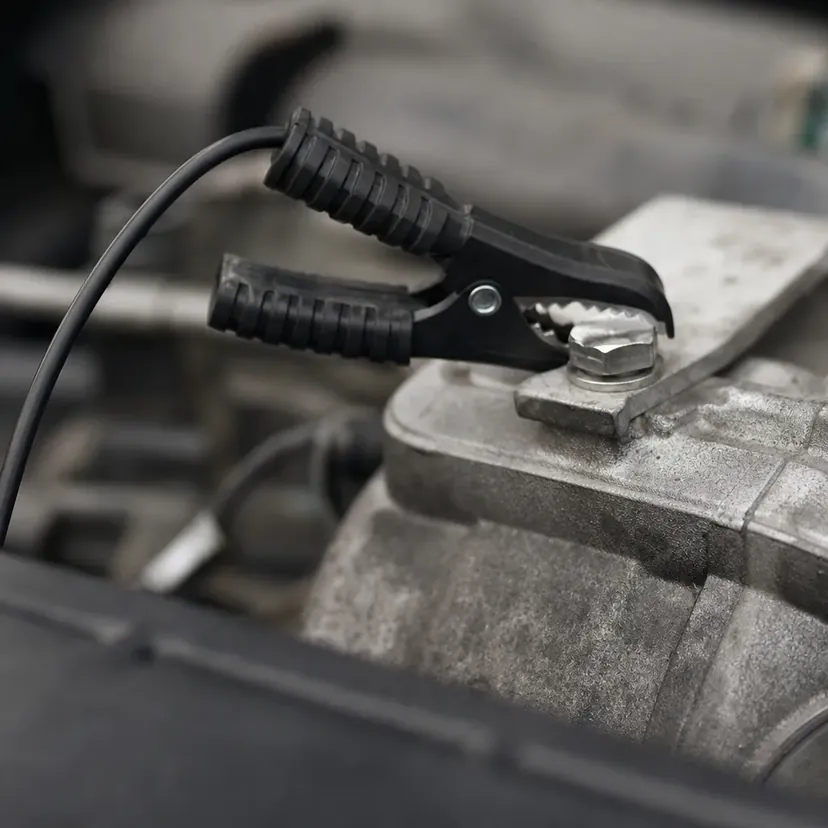 La pince noire d'un chargeur serrée sur une patte de masse boulonnée au bloc moteur.