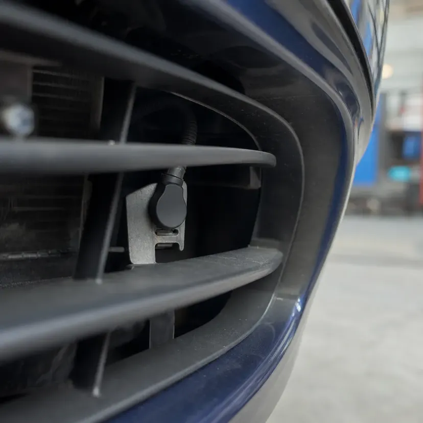 Capteur de température extérieure clipsé derrière les lames de la grille du bouclier avant, vu depuis l'extérieur du véhicule