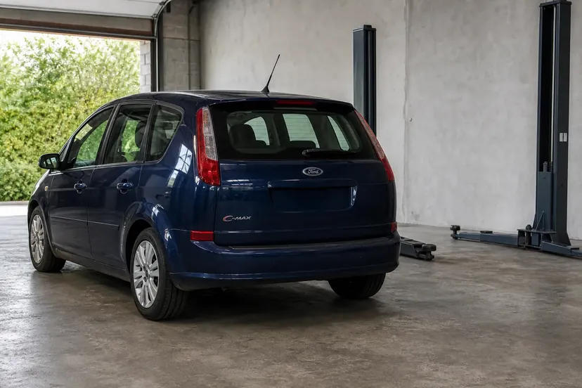 Ford C-Max bleu foncé vue de trois quarts arrière, garée dans une travée d'atelier devant un pont élévateur à deux colonnes vide