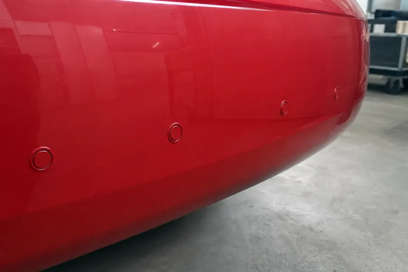 Plan rapproché sur un bouclier arrière rouge : quatre pastilles rondes de capteurs de stationnement peintes de la couleur de la carrosserie.