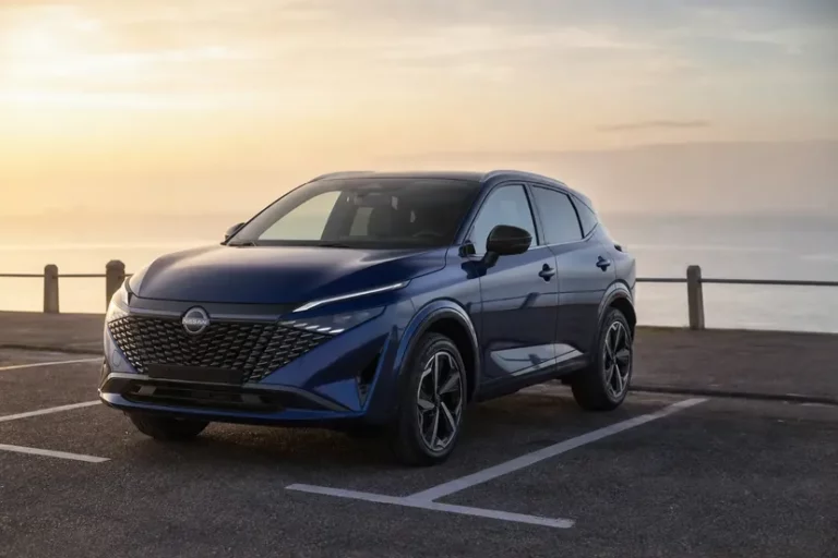 Nissan Qashqai J12 restylé bleu métallisé, vu de trois quarts avant, garé en épi sur un parking de front de mer au petit matin.