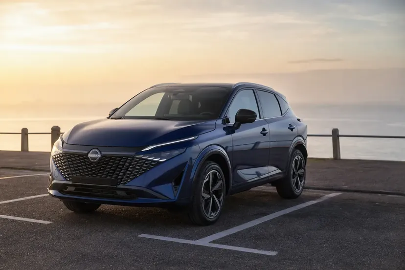 Nissan Qashqai J12 restylé bleu métallisé, vu de trois quarts avant, garé en épi sur un parking de front de mer au petit matin.