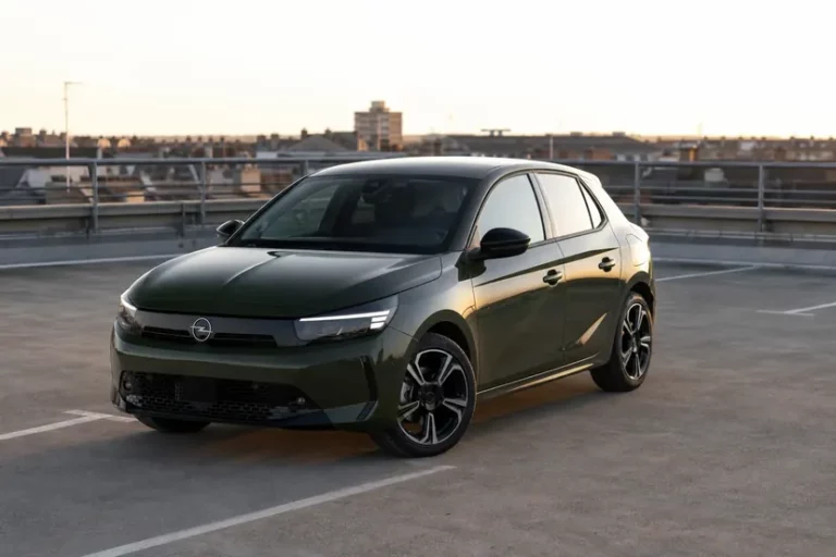 Opel Corsa F restylée vert olive, vue de trois quarts avant, garée seule sur le toit-terrasse d'un parc de stationnement, sous une lumière rasante.