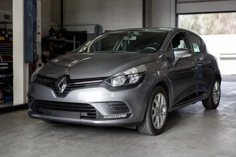 Une Renault Clio 4 grise vue de trois quarts avant, garée dans un atelier.