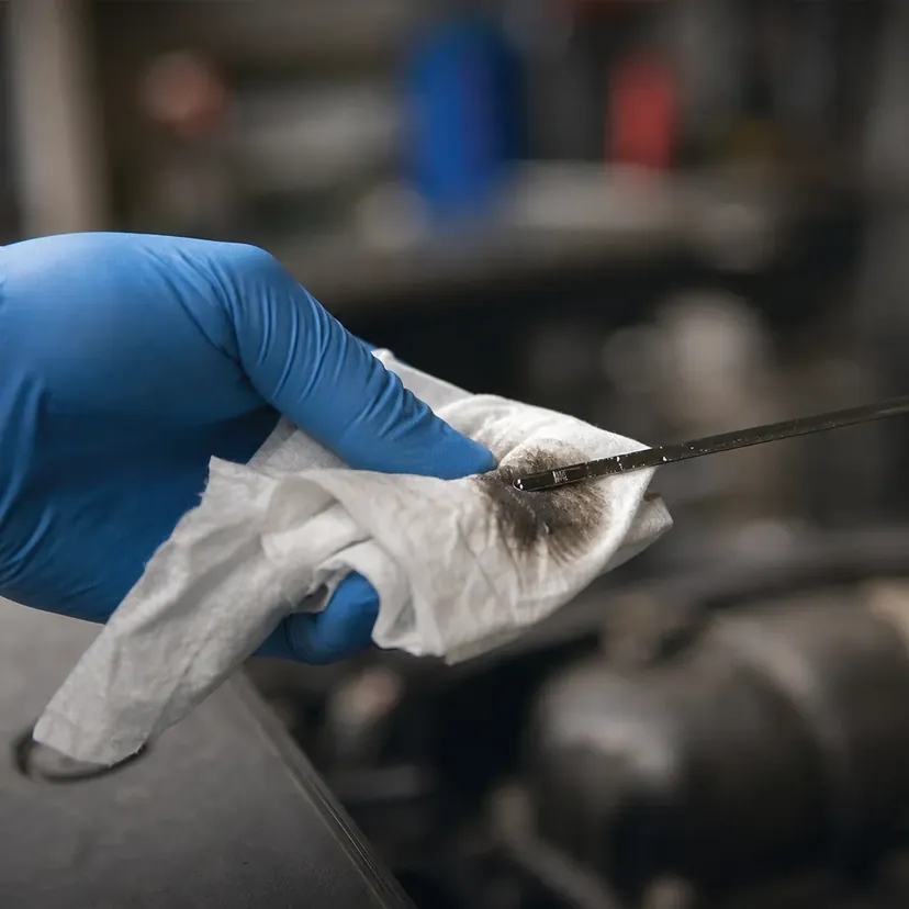 Une main en gant nitrile essuie avec un chiffon la tige de contrôle du niveau d'huile sortie du moteur d'une citadine