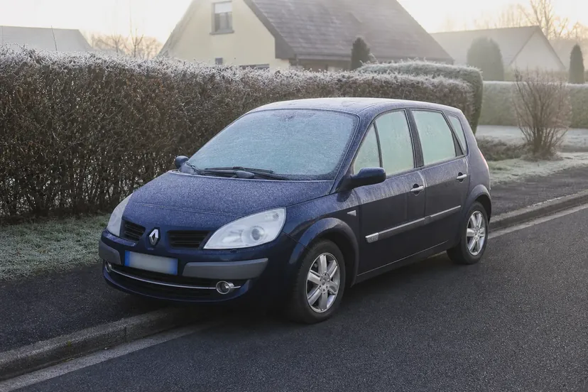 Renault Scénic II bleu marine garé dans une rue pavillonnaire, pare-brise, toit et capot couverts de givre, un matin d'hiver.