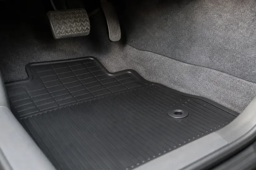 Plancher côté conducteur vu par la portière ouverte, tapis de caoutchouc noir à plat et accroché sous la pédale d'accélérateur