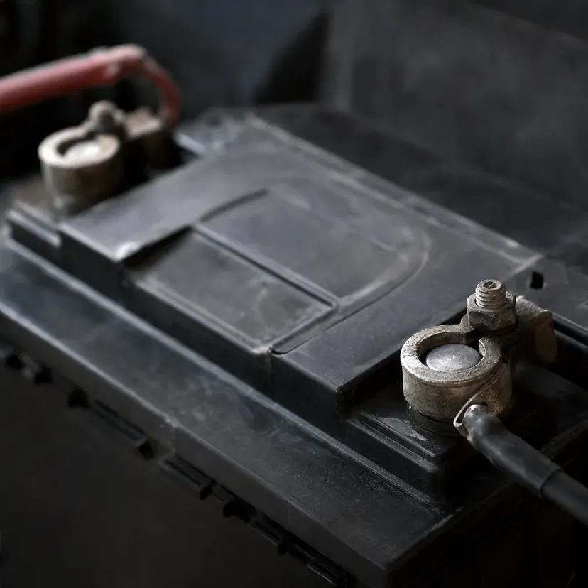 Gros plan sur les cosses d'une batterie de voiture, capot ouvert, dans un atelier automobile.