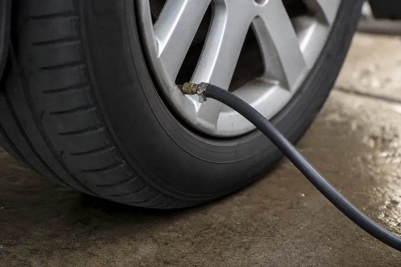 Un flexible de gonflage raccordé à la valve d'une roue de voiture posée au sol, dans un atelier automobile.