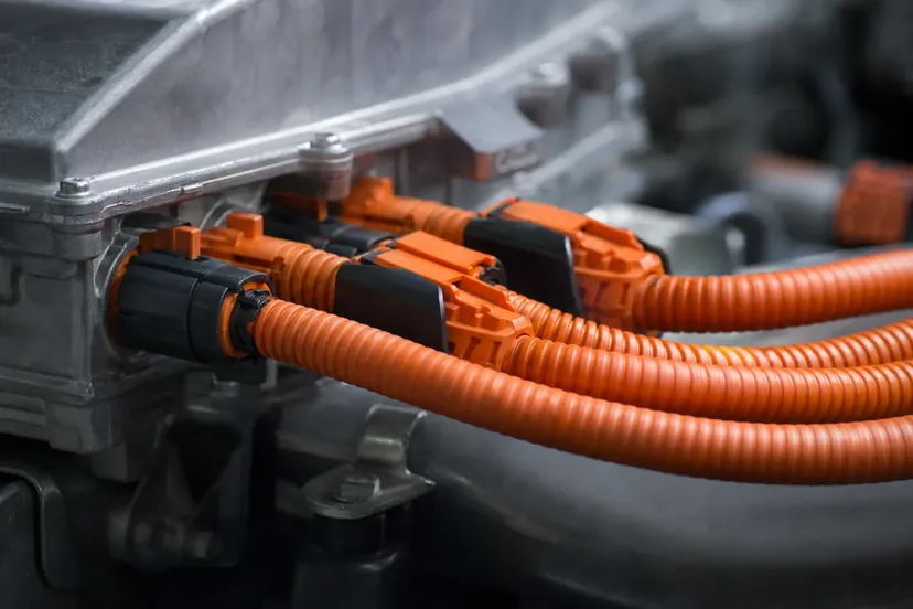 Un faisceau de câbles orange de circuit haute tension raccordé à un boîtier de puissance, vu en gros plan dans un atelier.